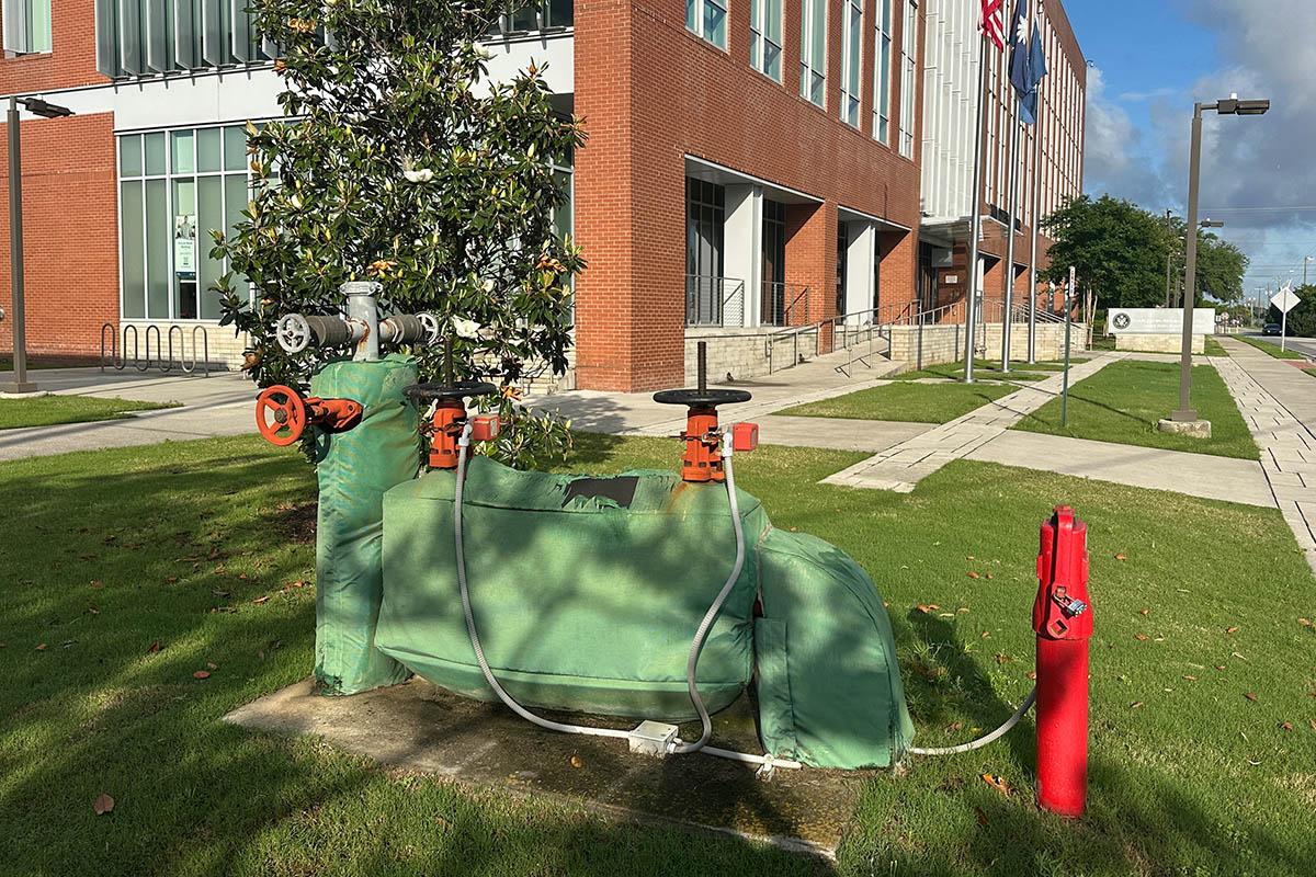 A large insulated commercial backflow prevention assembly on the lawn outside a brick office building