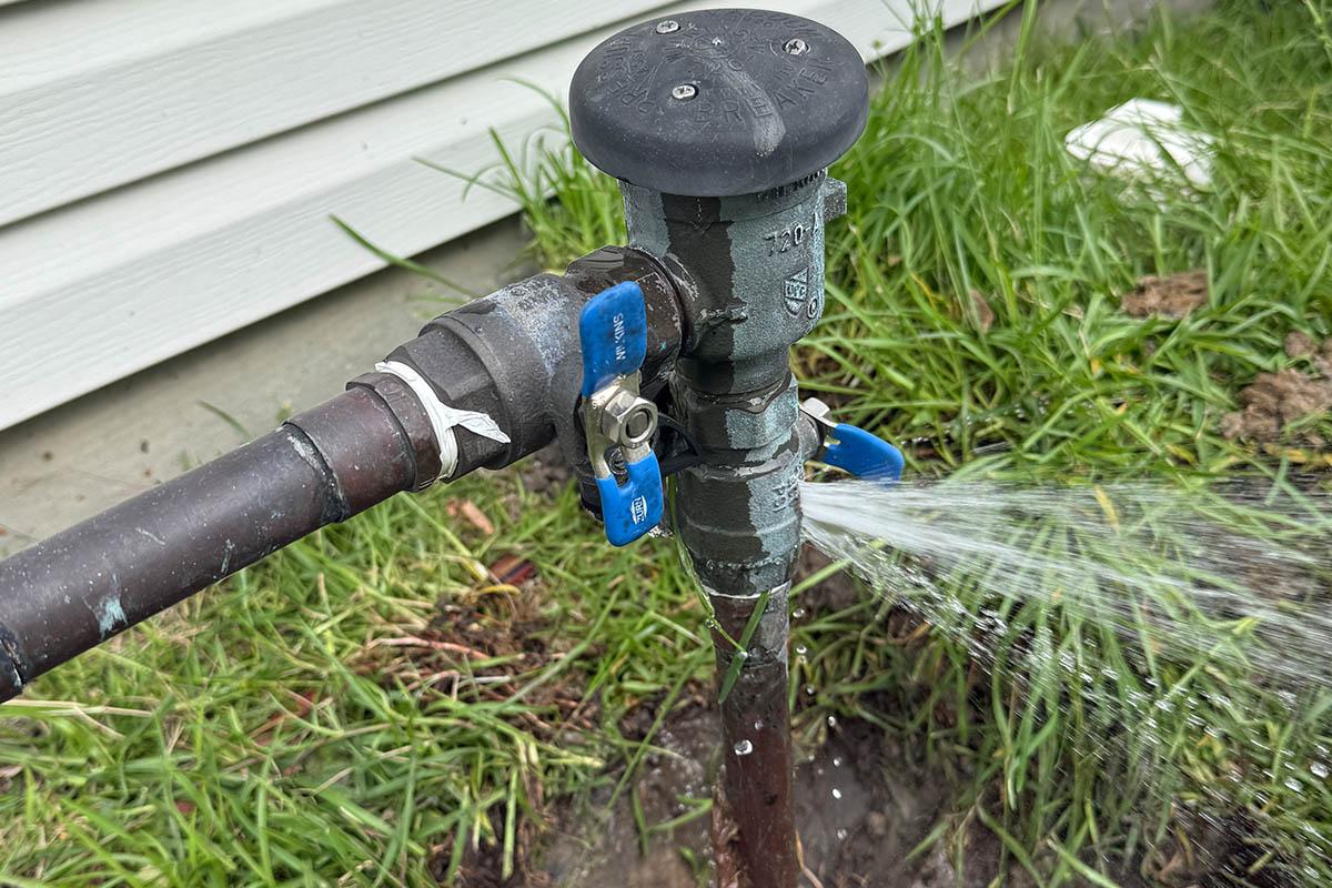 A failed backflow prevention assembly spraying water from its relief port onto the ground
